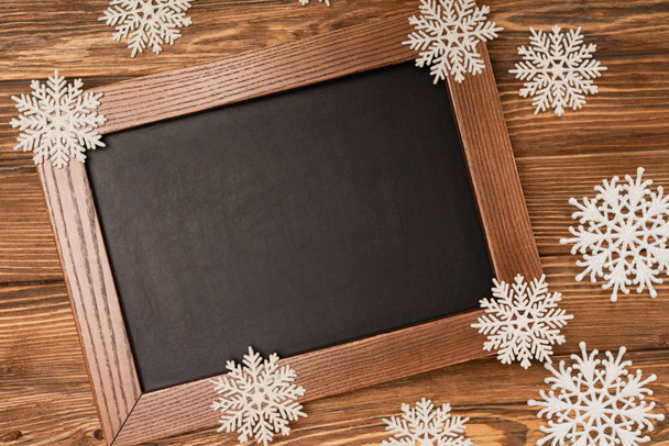 top view of winter snowflakes on chalkboard on wooden background - Foto, imagen