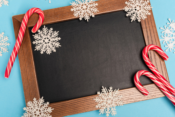 top view of chalkboard, candy canes and snowflakes on blue background - Valokuva, kuva