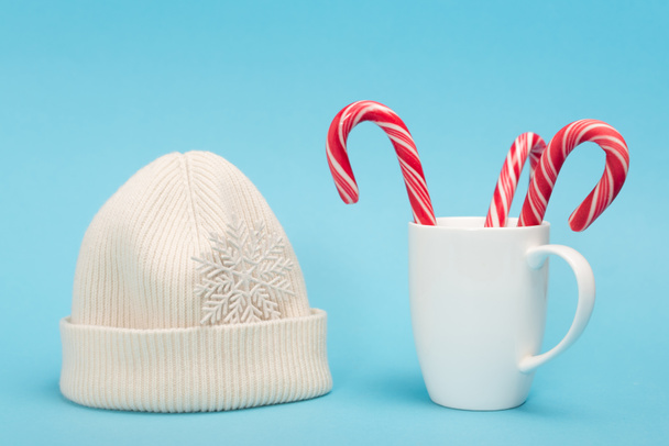 white beanie and candy canes in mug on blue background - Photo, Image