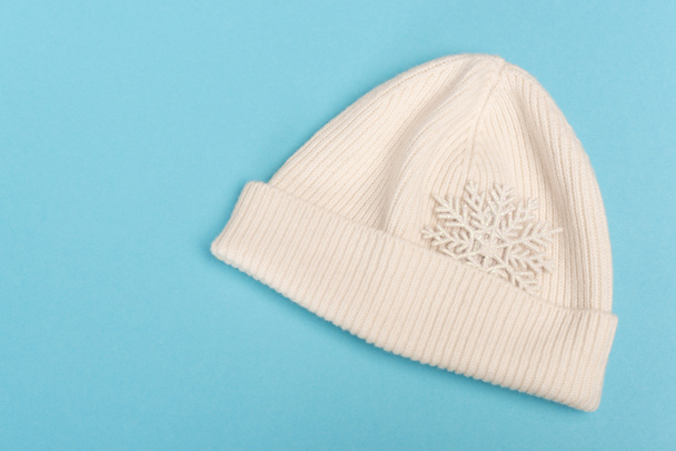 top view of white beanie and snowflake on blue background - Φωτογραφία, εικόνα
