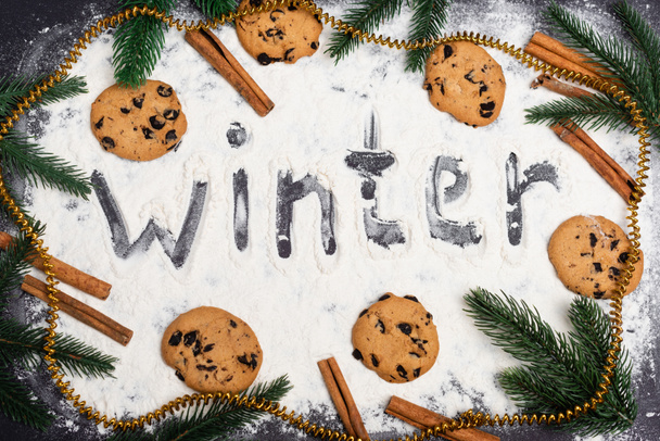 vue du dessus du mot hiver, branches de sapin et biscuits au chocolat sur fond noir - Photo, image