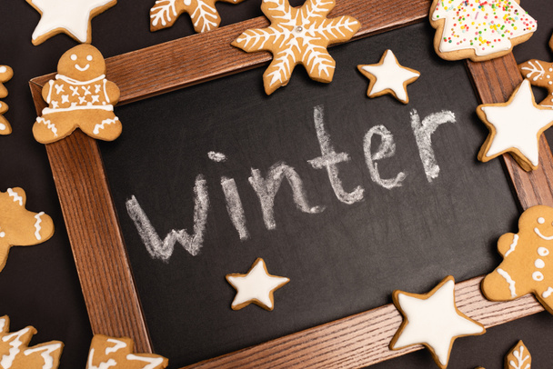 верхний вид пряничного печенья и слово зима на доске на черном фоне - Фото, изображение