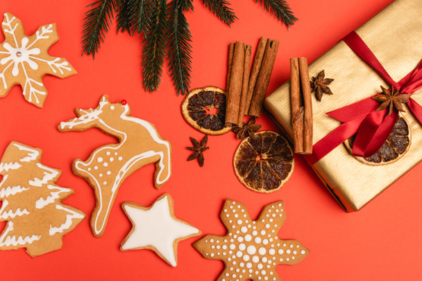 vrchní pohled na vánoční stromek, dárek s kořením a perníkové sušenky na červeném pozadí - Fotografie, Obrázek