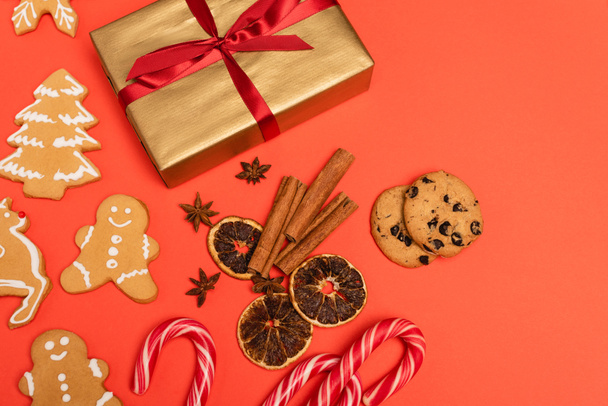 top view of gift, candy canes, spices and gingerbread cookies on red background - Photo, Image
