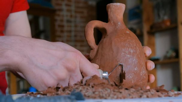 Alfarero profesional moldeando tarro de arcilla seca con herramienta especial en taller de cerámica - Foto, imagen