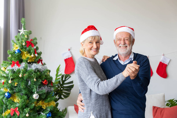 Senioren-Paar tanzt fröhlich im Wohnzimmer, das in der Weihnachtszeit mit dem Weihnachtsbaum geschmückt ist - Foto, Bild