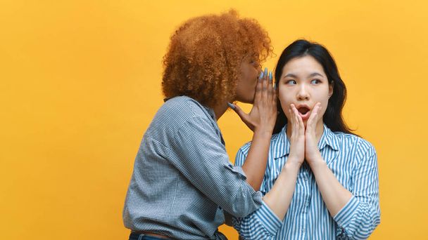 Young african american black woman whisperingto her asian friend expressing shock. gossip girls and secrets - Zdjęcie, obraz