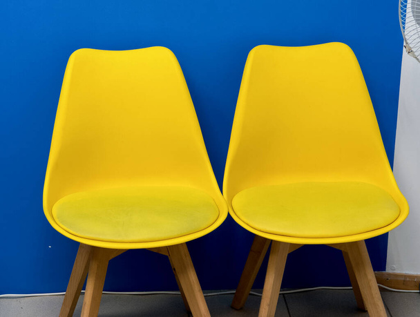 Dwa kolorowe żółte krzesła w klasie pod niebieską ścianą. Zamknij drzwi. Minimalna konstrukcja. - Zdjęcie, obraz
