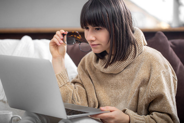 Dziewczyna w okularach patrzy na ekran laptopa z koncentracją. Koncepcja pracy zdalnej, freelancing. - Zdjęcie, obraz