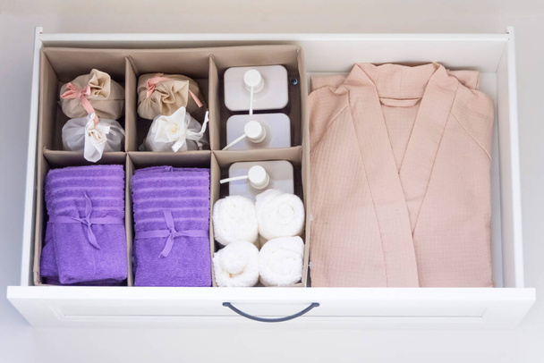 Συρτάρι μπάνιου, μπουρνούζι και λιλά πετσέτες, σαπούνι, πετσέτες χεριών και υγρά σαπούνια - Φωτογραφία, εικόνα