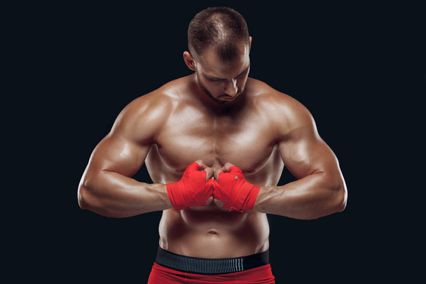 Front view of a sporty man in boxing gloves practicing fighting techniques isolated on black background - Фото, зображення