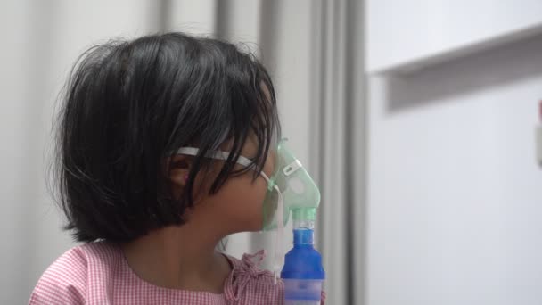 Kis ázsiai lány oxigénmaszkkal és porlasztón keresztül lélegzik a kórházban. A bronchitis, a légzőszervi és orvosi kezelés fogalma. - Felvétel, videó