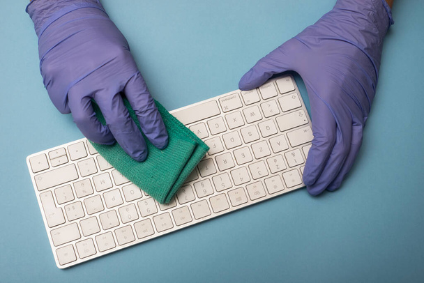 closeup of hands of man with latex gloves cleaning a computer keyboard on blue color background - Фото, изображение