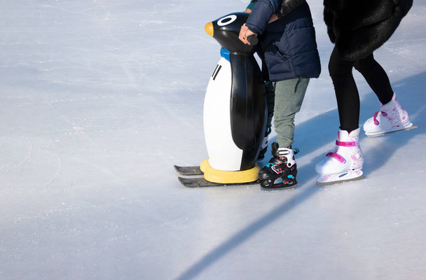 Ledové kluziště. Máma učí dítě bruslit. Chlapec drží tučňáka jako oporu. Zimní čas, rodinné aktivity a sportovní koncept. Vánoční prázdniny, zábava v mrazivý den pro děti a rodiče. kopírovat prostor - Fotografie, Obrázek