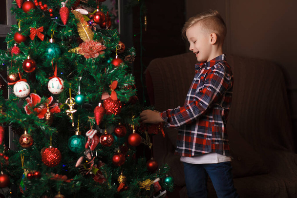 Mały chłopiec stoi w pobliżu choinki posiada duże prezenty noworoczne. Dziecko jest szczęśliwe z prezentem noworocznym. Szczęśliwego Nowego Roku. Portret. Śmieszne zdjęcie. - Zdjęcie, obraz