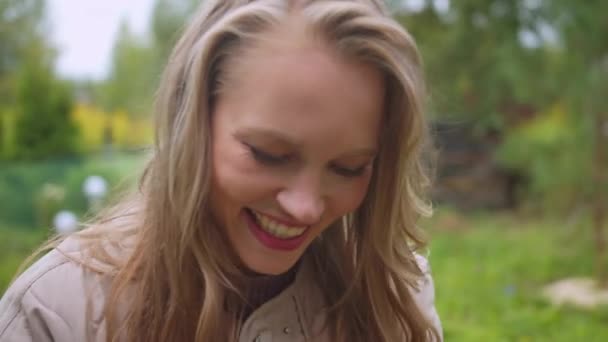 Young blonde woman in nature laughing and flipping through photos on her smartphone - Footage, Video
