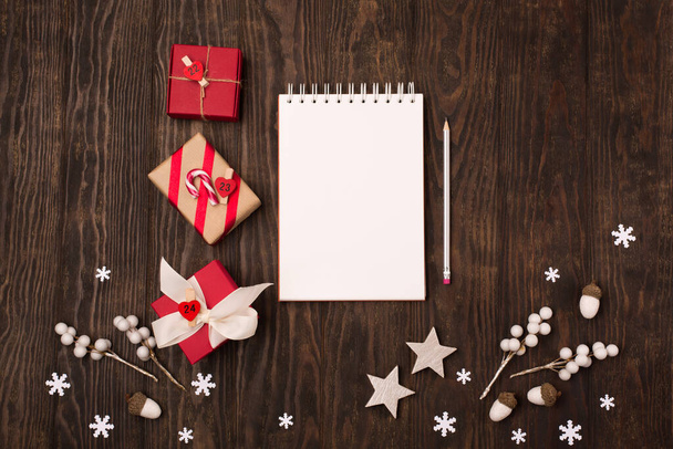 クリスマスのグリーティングカード。空の白いノートブック、クリスマスの装飾、暗い木製の背景に雪片。フラットレイアウト、トップビュー、コピースペース. - 写真・画像