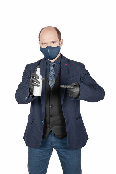 Beau jeune homme d'affaires avec masque de protection contre le virus médical chirurgical et gants noirs tenant une bouteille antiseptique isolée sur du blanc - Photo, image