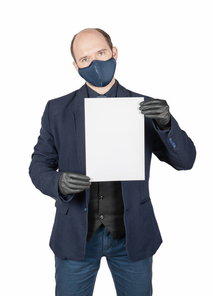 Hezký mladý obchodník s chirurgickou maskou proti virům a černými rukavicemi s prázdným listem papíru izolovaným na bílém - Fotografie, Obrázek