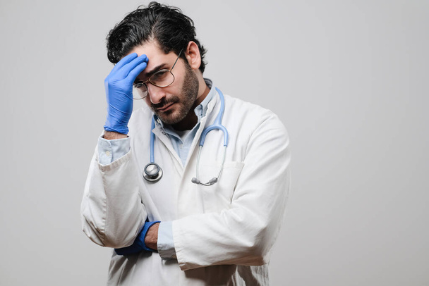 Vermoeide arts in wit uniform met bril en rubber blauwe handschoenen - Foto, afbeelding