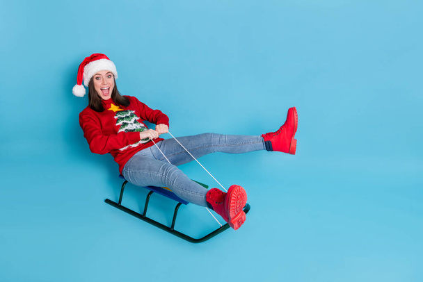Photo portrait of happy girl riding sledge isolated on pastel light blue colored background - Foto, afbeelding
