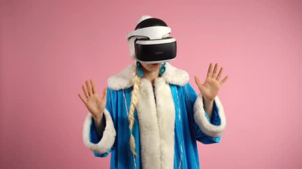 Mujer joven con gafas de realidad virtual modernas de pie sobre un fondo rosa aislado. Mujer concentrada está inmersa en videojuegos VR, realidad virtual 3D en interiores. Auriculares de realidad virtual aumentada - Imágenes, Vídeo