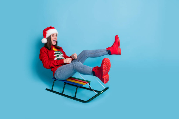 Photo portrait of woman riding sleigh with legs up screaming laughing isolated on pastel light blue colored background - Foto, imagen