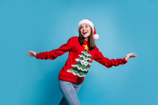 Photo of lovely cute lady excited look back empty space toothy beaming smile hands wear santa x-mas headwear red ornamented pullover jeans isolated blue color background - Foto, immagini