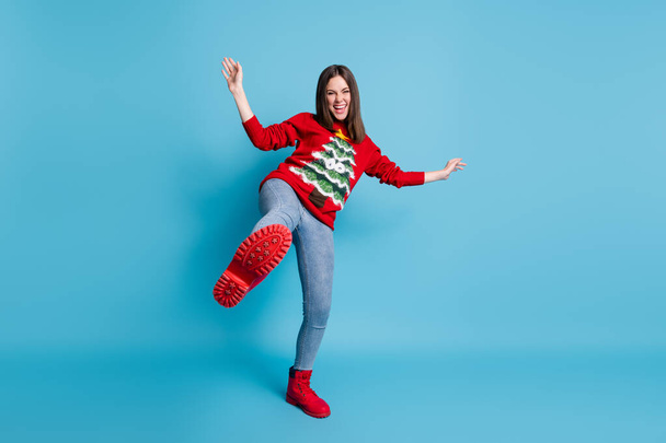 Full length body size photo of funny demale student playing fooling standing on one leg laughing showing red shoe wearing xmas sweater isolated on blue color background - Fotó, kép