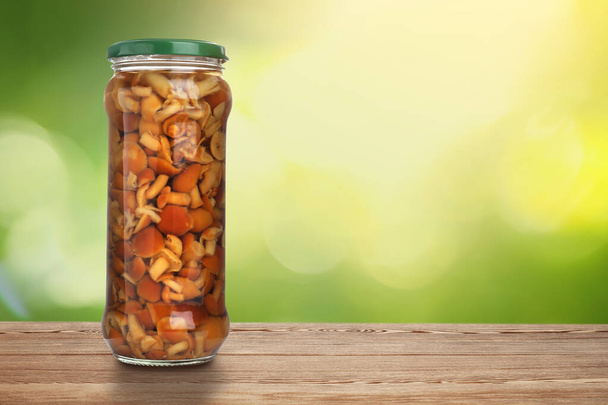 Jar of pickled mushrooms on wooden table against blurred background, space for text - Foto, afbeelding