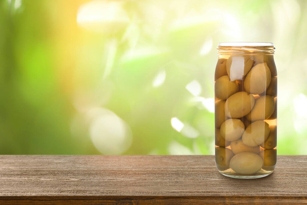 Jar of pickled olives on wooden table against blurred background, space for text - Fotoğraf, Görsel