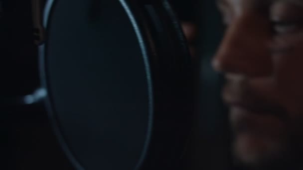 Πορτρέτο του όμορφου αρσενικού rap τραγουδιστή σε ακουστικά με επαγγελματικό μικρόφωνο τραγουδώντας νέο τραγούδι στο σύγχρονο στούντιο. Μουσική παραγωγή. Κακό φως - Πλάνα, βίντεο