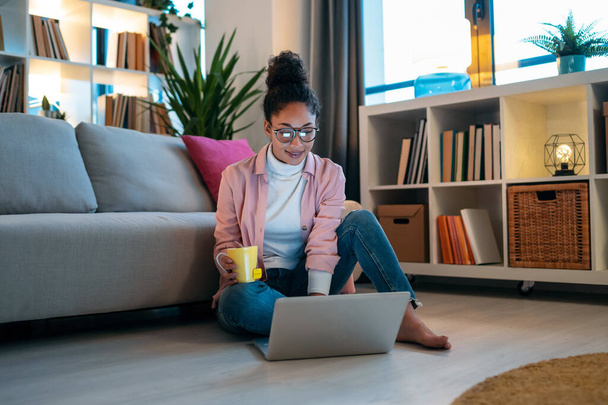 Shot of attractive happy young entrepreneur woman working with laptop while drinking a cup of coffee sitting on the floor in the office. - Foto, imagen