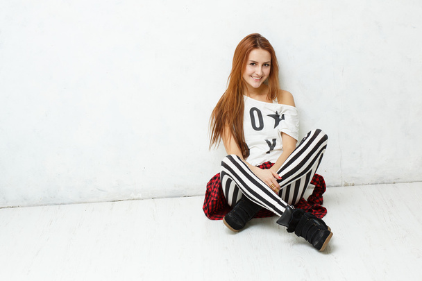 Young, stylish girl posing sitting on a white floor against a wh - Photo, Image