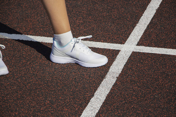 athlete's foot in sneakers starts from white stripe on asphalt pavement. - Photo, Image