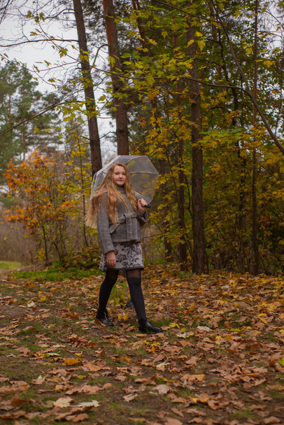 cute beautiful teenage brunette girl in an orange hat, dress and coat walking with a transparent umbrella. Cosiness, autumn. - Fotó, kép