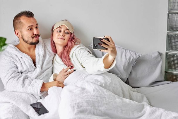 couple on bed take photo on smartphone - Foto, afbeelding