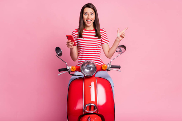 Portrait of her she nice attractive lovely amazed stunned cheerful girl riding moped using device demonstrating copy empty space new novelty isolated over pink pastel color background - Fotografie, Obrázek