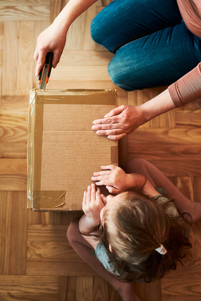 Woman unpacking a cardboard box parcel in room at home. Little girl waiting for opening a gift in package - Fotó, kép