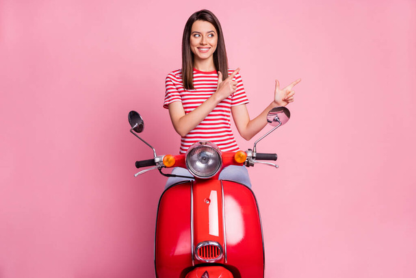 Photo of positive optimistic cute young lady ride bike dress red white t-shirt point empty space isolated on pink background - 写真・画像