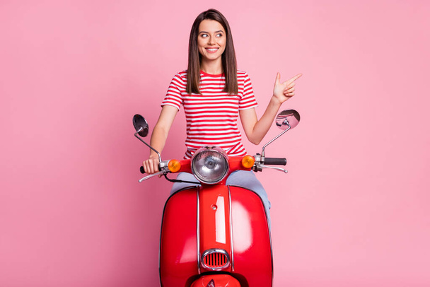 Photo portrait of curious girl sitting on red motorcycle pointing at empty space smiling isolated on pastel pink color background - Foto, immagini