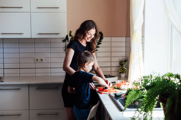 Maman et jeune fils coupent des légumes pour la salade dans la cuisine - Photo, image