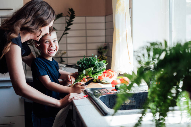 Maman et jeune fils coupent des légumes pour la salade dans la cuisine - Photo, image