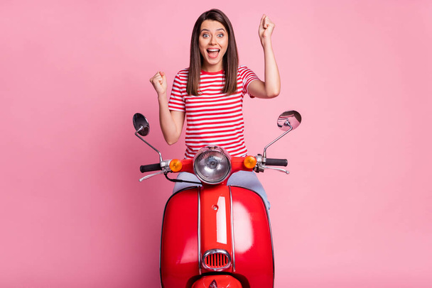 Photo portrait of female driver sitting on red motorcycle gesturing like winner isolated on pastel pink color background - Photo, image