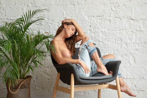 молодая красивая женщина позирует обнаженной в студии, сидя в джинсах - Фото, изображение