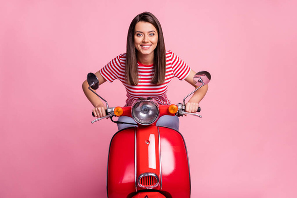 Photo portrait of young girl driving red motorbike smiling wearing striped t-shirt isolated on pastel pink color background - Photo, Image