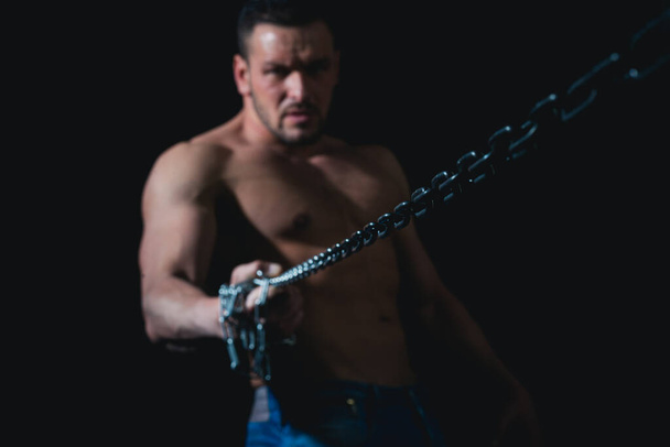 Guy on black with strained muscles holds a rusty metal chain, a concept of strength man power. - Foto, immagini