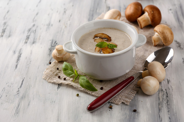Mushroom soup in white pot, on napkin, on wooden background - Foto, afbeelding
