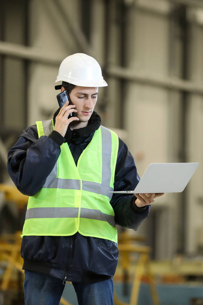  Portret van een man, fabrieksingenieur in werkkleding met laptop en telefoon, die het werkproces bij de helikopterfabrikant controleert. - Foto, afbeelding