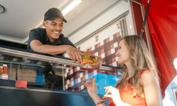Cook in a food truck handing tasty burger over to woman customer - Photo, Image